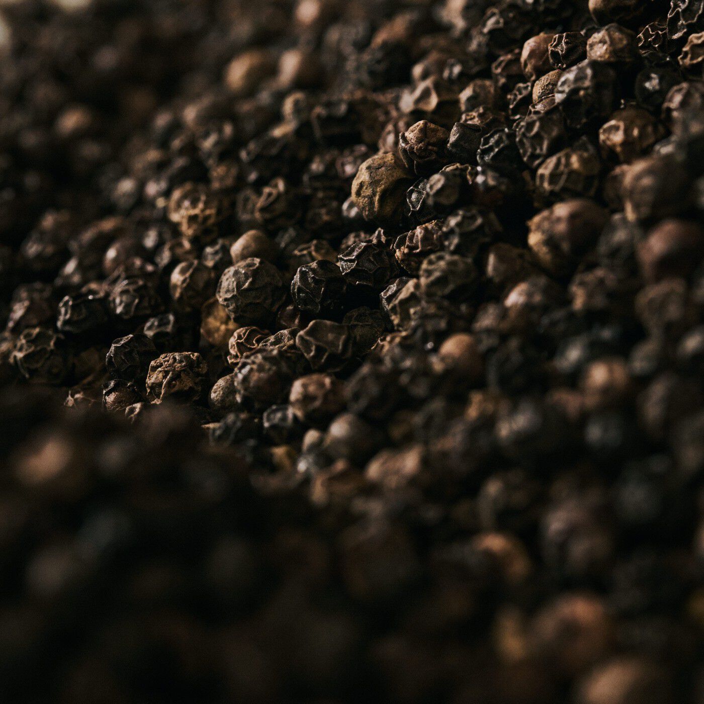 Close-up of black peppercorns scattered across a dark textured surface.