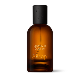 Amber glass Aesop Journey to Ouranon Eau de Parfum bottle with black cap on a white background.
