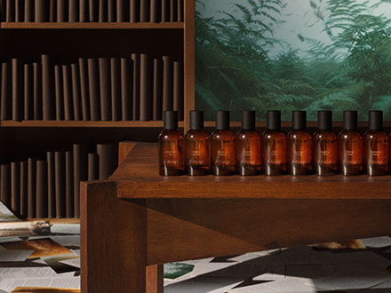 Flacons en verre ambre alignes sur une table en bois dans une piece avec une bibliotheque et une fresque de foret.