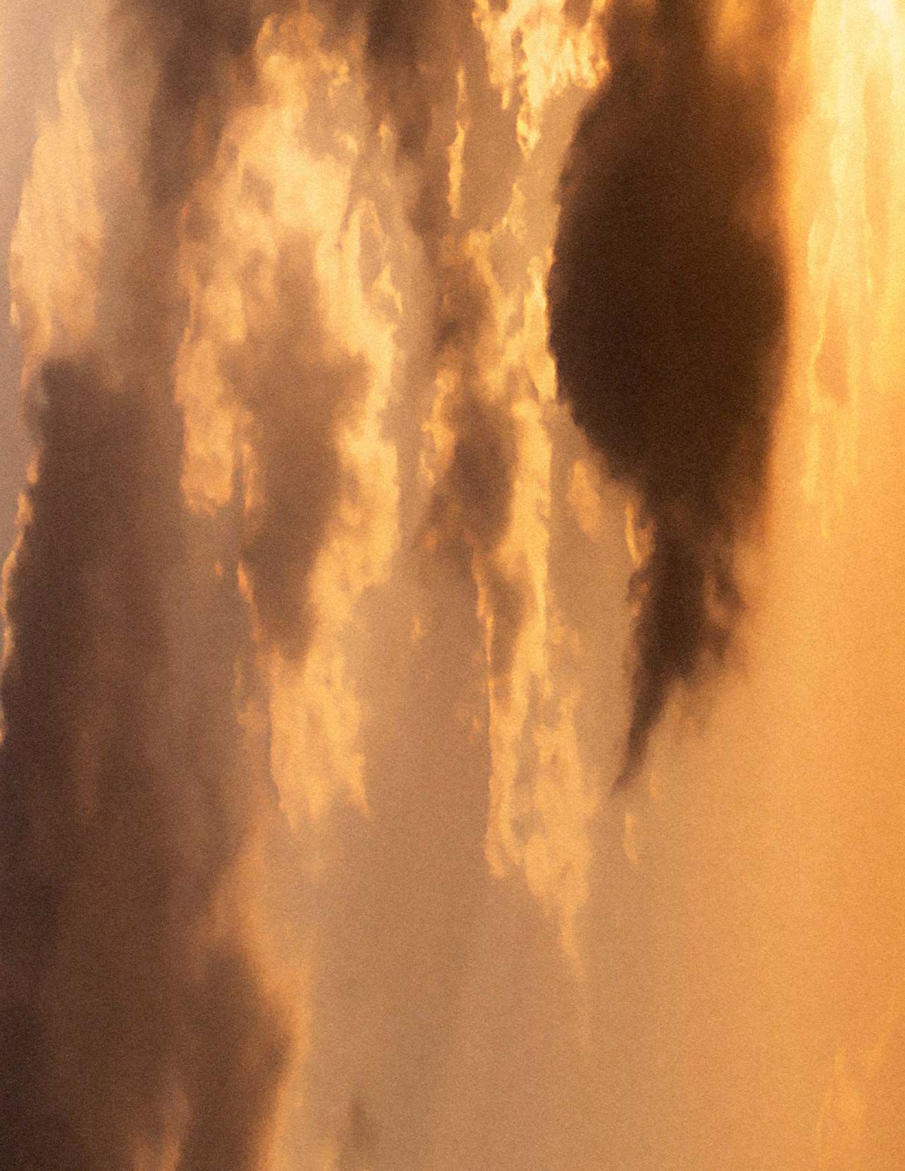 Ciel de coucher de soleil dore, aux nuages superposes dans des tons ambres chaleureux, baigne d’une lumiere douce et diffuse, et traverse de formations nuageuses plus sombres.
