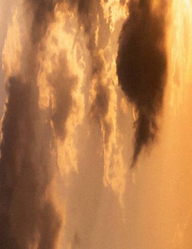Ciel de coucher de soleil dore, aux nuages superposes dans des tons ambres chaleureux, baigne d’une lumiere douce et diffuse, et traverse de formations nuageuses plus sombres.