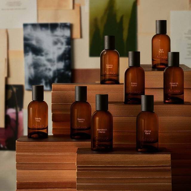 Collection de flacons de fragrances ambrees disposes sur des blocs de bois, devant des estampes et papiers superposes aux tons creme feutre et charbon.