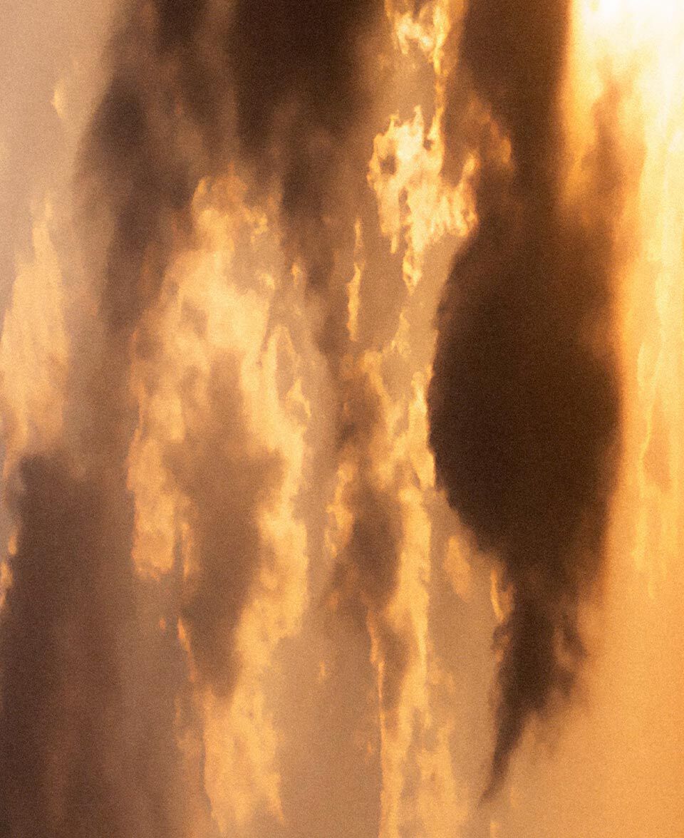 Un nuage lumineux se forme dans une chaude lumiere orangee, evoquant la fumee et un ciel eclaire par le feu.
