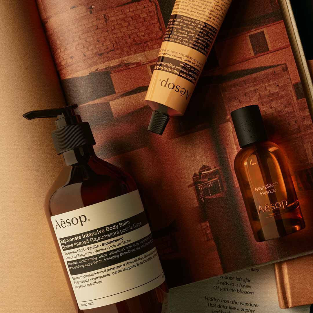 Flacon Aesop Marrakech Intense avec flacon-pompe et tube jaune, disposes sur des papiers aux tons chauds.