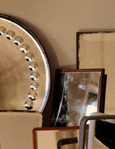 Objets metalliques et mineraux empiles, dans des tons bronze, beige et brun fonce, composes de formes geometriques superposees sur fond de mur neutre.