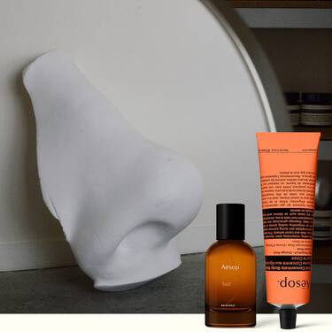 Amber perfume bottle and coral hand cream beside a white sculpture