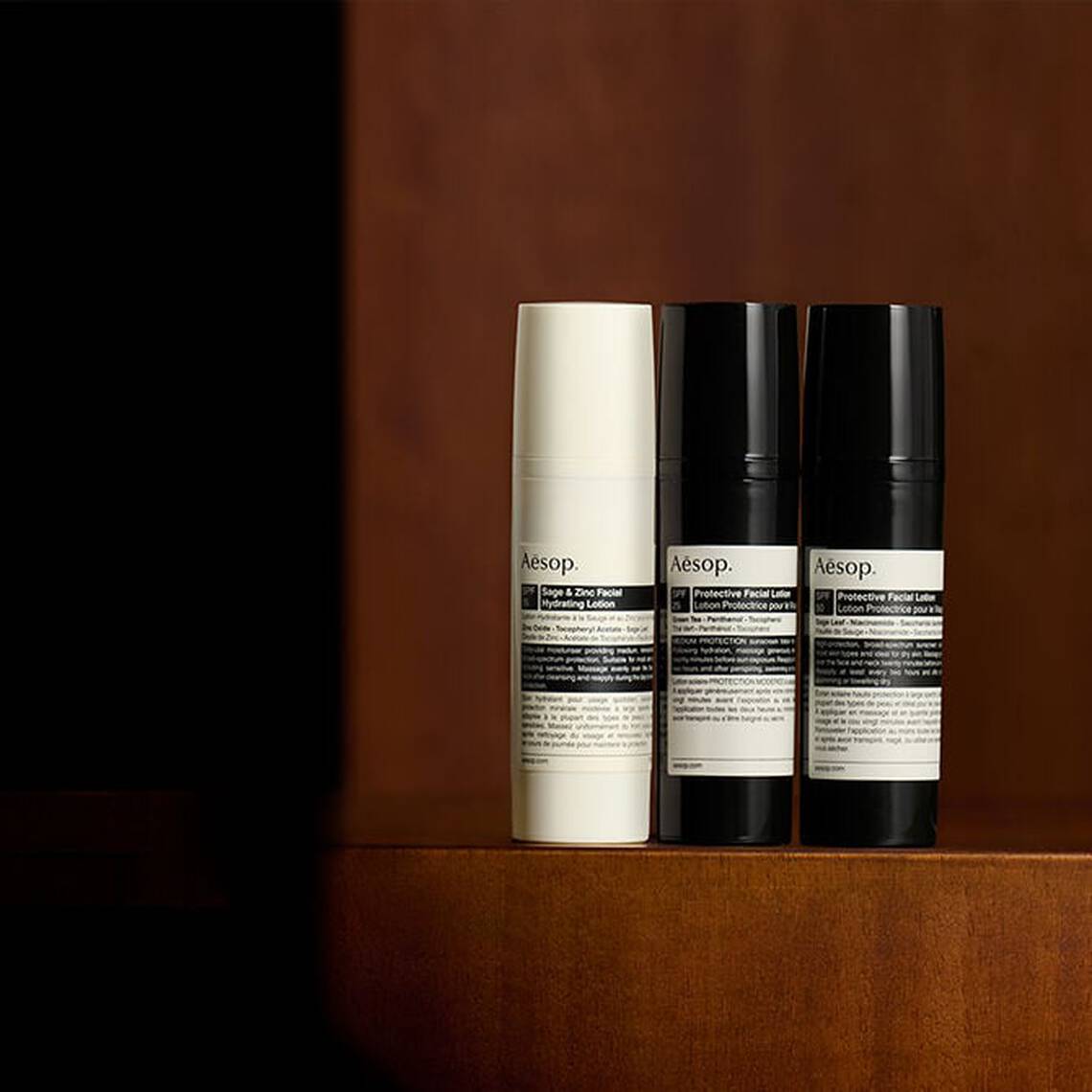 Une selection soignee de formulations de protection solaire Aesop posees sur une surface en bois sombre dans un cadre doucement eclaire.