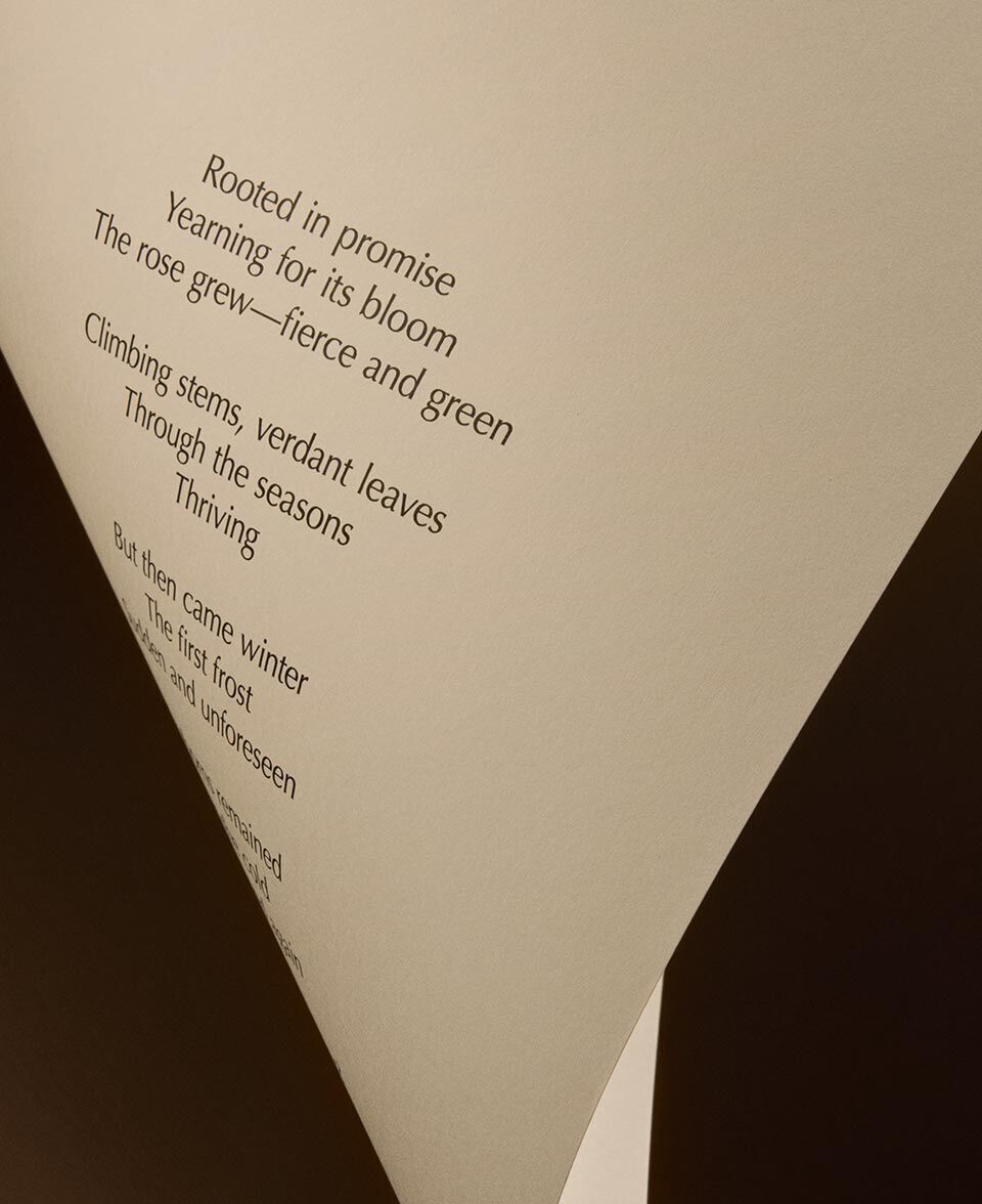Pli triangulaire de papier creme presentant le texte d’un poeme sur fond sombre.